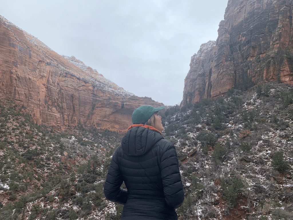 Hiker in Zion National Park in the winter. There is snow on the ground, but the hiker is wearing a warm down coat. 